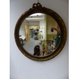 AN ROUND MIRROR IN GILT FRAME CRESTED BY RIBBON TIED FRONDS.