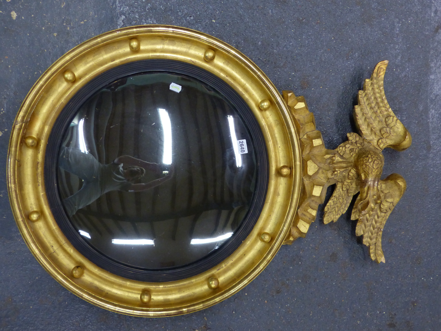 A CONVEX MIRROR WITHIN REEDED SLIP AND BEADED GILT FRAME SURMOUNTED BY AN EAGLE. H 90 x Dia. 63cms.