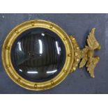 A CONVEX MIRROR WITHIN REEDED SLIP AND BEADED GILT FRAME SURMOUNTED BY AN EAGLE. H 90 x Dia. 63cms.