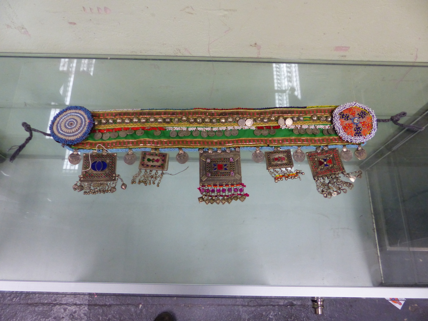 AN ISLAMIC BEADED TEXTILE BELT SEWN WITH 1990S TURKISH COINS AND HUNG WITH COLOURED PASTE MOUNTED