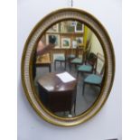 AN OVAL MIRROR WITHIN GILT BEAD AND FLUTED WHITE BANDS ON THE GILT EDGED FRAME. H 80 x 62.5cms.