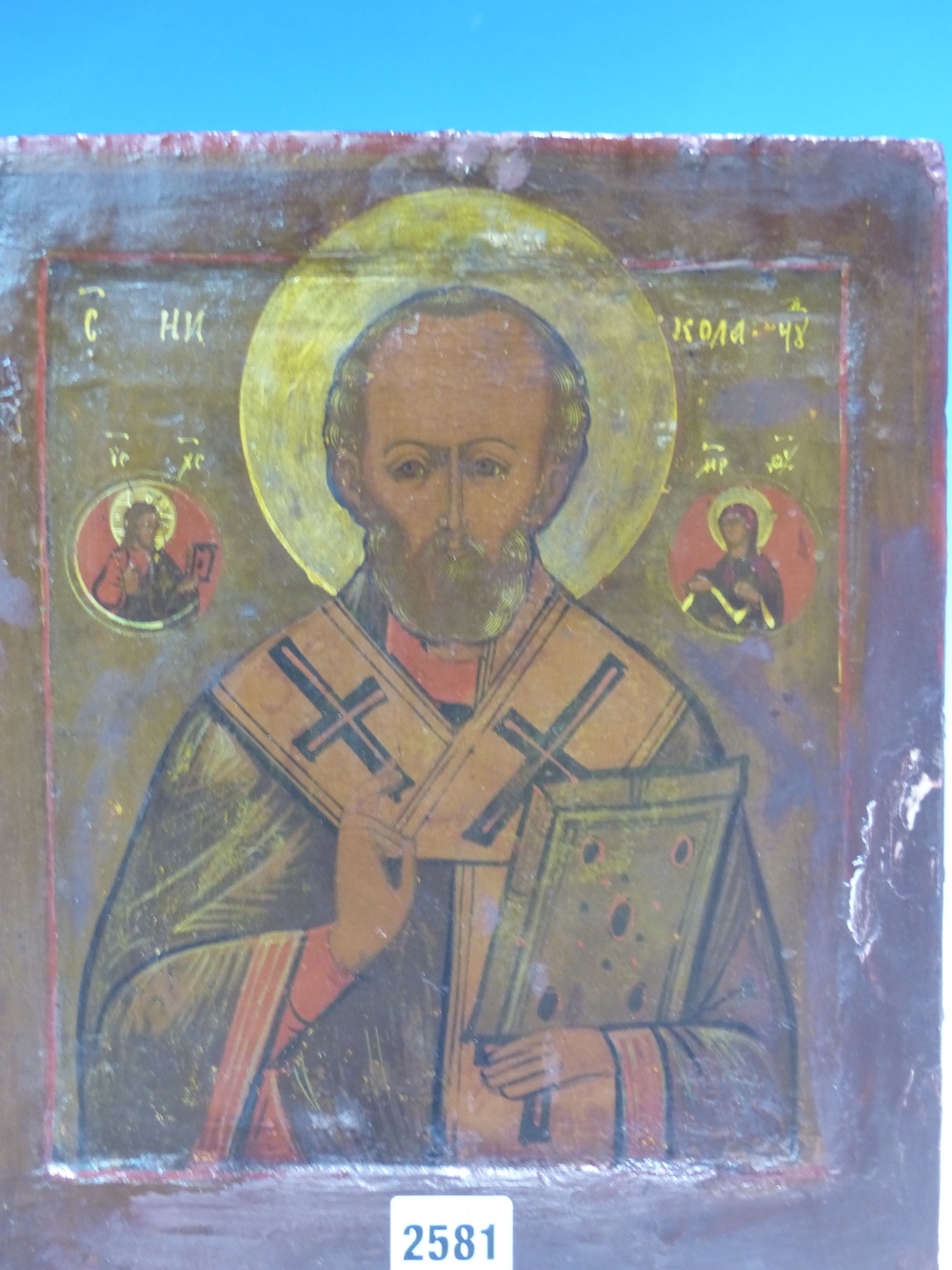 A RUSSIAN ICON PAINTED WITH ST NICHOLAS HOLDING A HOLY BOOK, ROUNDELS OF ST MARY AND JESUS ABOVE HIS