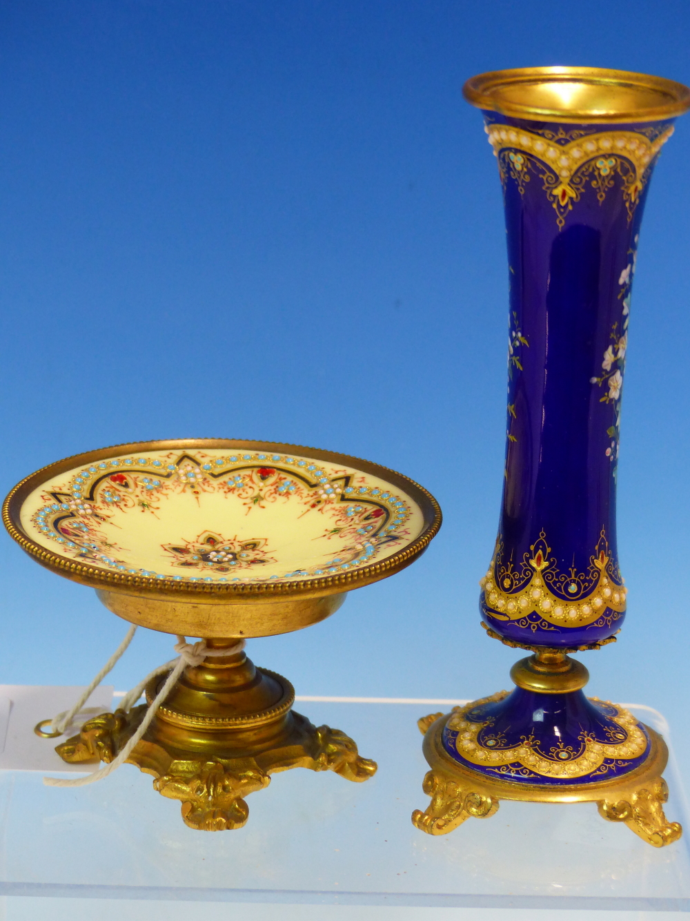 A FLORAL ENAMELLED ROYAL BLUE GROUND WAISTED CYLINDRICAL VASE ON FOUR ORMOLU FEET. H 15cms. ROGETHER