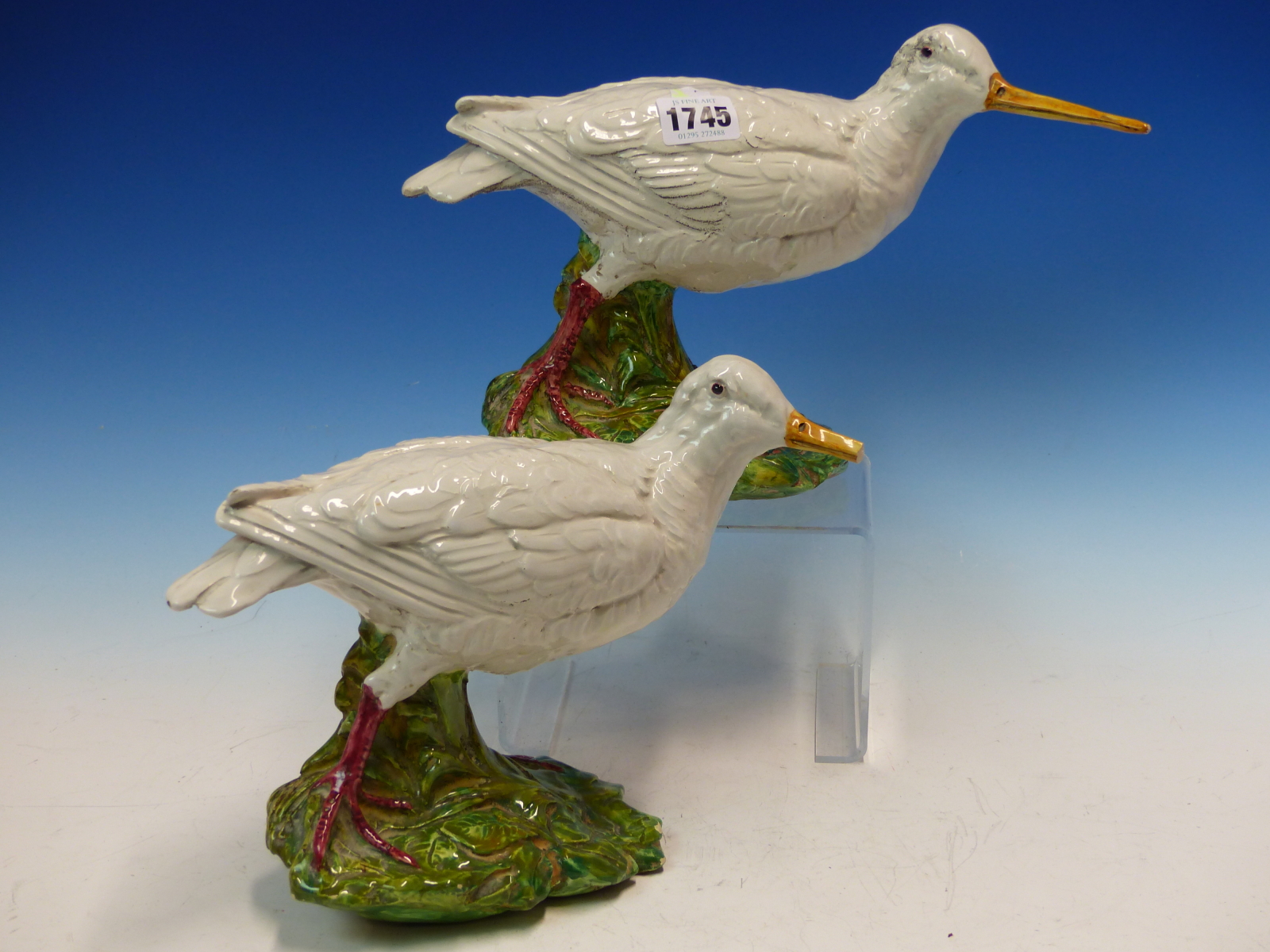 A PAIR OF MAJOLICA WHITE WADING BIRDS WITH LONG YELLOW BEAKS, THEIR RED LEGS ON GREEN FOLIAGE