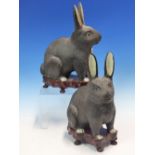 A PAIR OF JAPANESE PORCELAIN SEATED BLACK RABBITS AND WOOD STANDS. H 20cms.