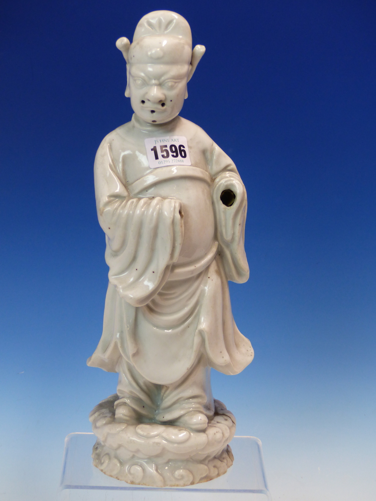 A BLANC DE CHINE FIGURE OF A FIERCE EYED MANDARIN STANDING ON A DOUBLE CLOUD PLINTH, HIS CHIN