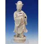 A BLANC DE CHINE FIGURE OF A FIERCE EYED MANDARIN STANDING ON A DOUBLE CLOUD PLINTH, HIS CHIN