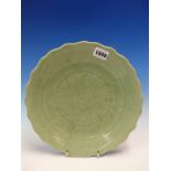 A CHINESE CELADON DISH INCISED TO DEPICT A LOTUS FLOWER WITHIN THE WAVY RIM. Dia. 26cms.