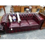 A BURGUNDY LEATHER BUTTON BACK CHESTERFIELD SOFA, AND SIMILAR FOOTSTOOL.