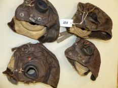 A COLLECTION OF FOUR BROWN LEATHER FLYERS HOODS, EACH WITH BLACK RUBBER EAR PIECES TO TAKE SOUND