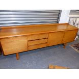 A TEAK SIDEBOARD, THE RECTANGULAR TOP SWEPT UP AT THE BACK AND ABOVE THREE DRAWERS AND CUPBOARDS