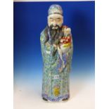 A CHINESE FIGURE OF FU XING STANDING IN GREEN GROUND FLORAL ROBES WITH A CHILD IN HIS ARMS. H