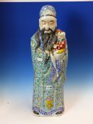 A CHINESE FIGURE OF FU XING STANDING IN GREEN GROUND FLORAL ROBES WITH A CHILD IN HIS ARMS. H