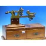 M COHEN LEEDS, A BRONZE AND STEEL WATCHMAKERS LATHE MOUNTED ON AN OAK BOX WITH TWO DRAWERS