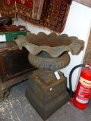 A PAIR OF CAST IRON URNS ON FLARING SQUARE SECTION BASES, THE FRILLED RIMS ABOVE GADROONED ROUNDED