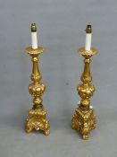 A PAIR OF GILT COMPOSITION BAROQUE STYLE CANDLESTICK LAMPS, THE BALUSTER COLUMNS ABOVE FRUIT KNOPS