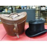 A RED SILK LINED LEATHER TOP HAT CASE CONTAINING A MOSS BROS. TOP HAT WITH BLACK SILK PILE, THE