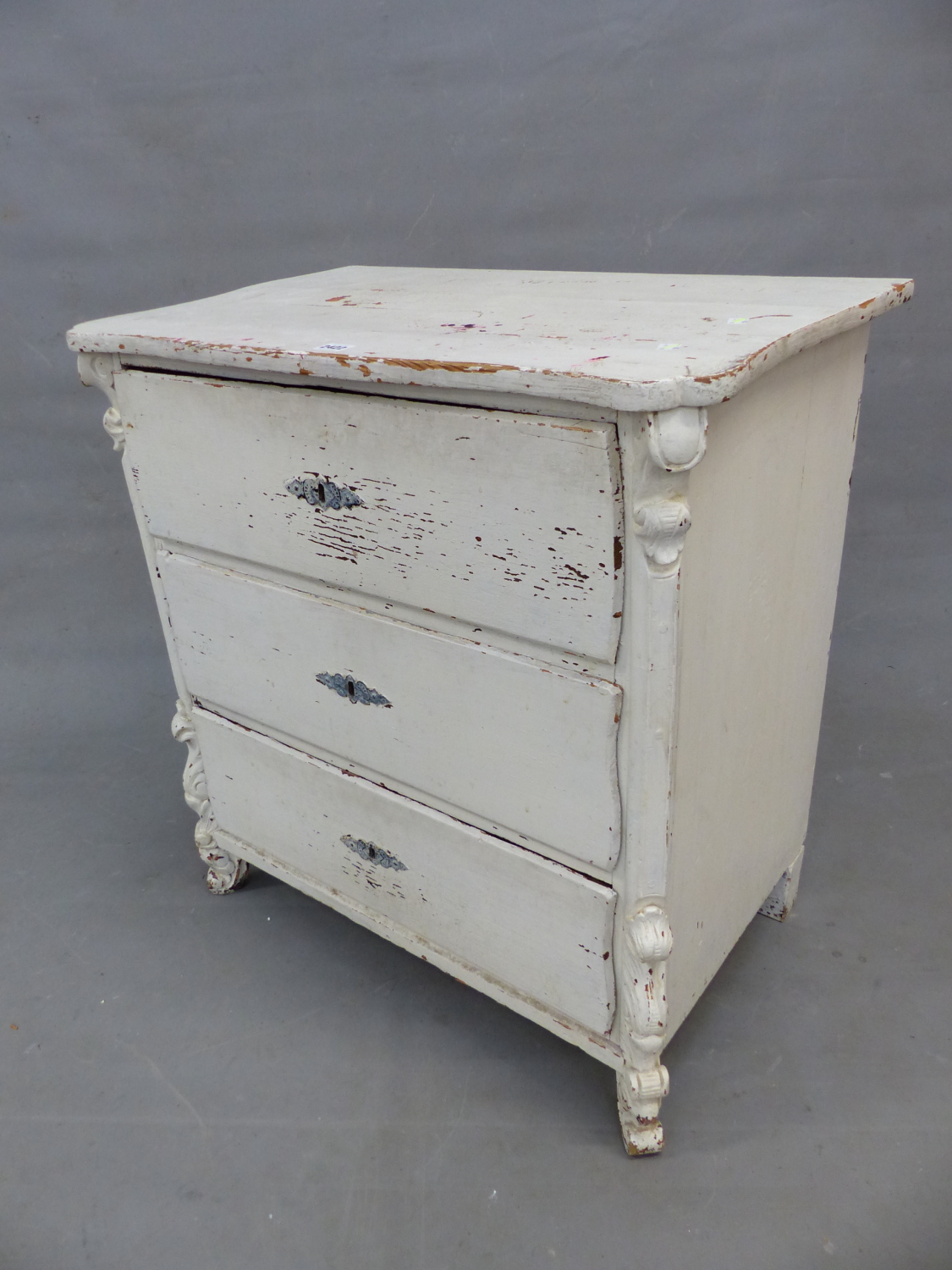 A 19th C. PAINTED PINE CHEST OF THREE DRAWERS BELOW A SERPENTINE FRONTED TOP AND ON FOLIATE CARVED