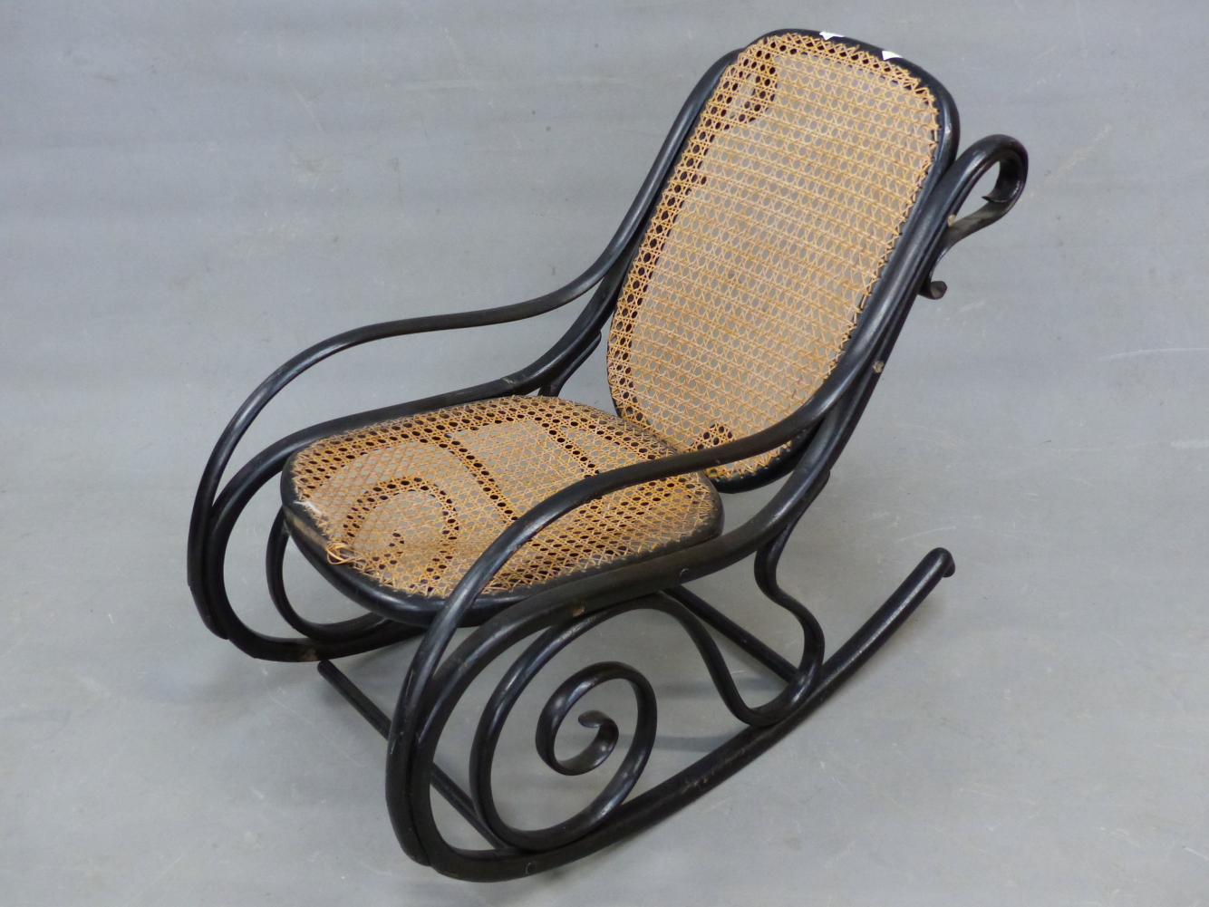 A THONET STYLE EBONISED BENT WOOD ROCKING CHAIR WITH CANED BACK AND SEAT