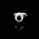 AN 18ct GOLD SAPPHIRE AND DIAMOND CLUSTER RING. THE OVAL CUT CLAW SET SAPPHIRE SURROUNDED BY A