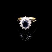 AN 18ct GOLD SAPPHIRE AND DIAMOND CLUSTER RING. THE OVAL CUT CLAW SET SAPPHIRE SURROUNDED BY A