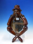 AN OVAL MIRROR IN MAHOGANY FRAME CARVED AS AS SEATED MAN HEAD IN HANDS AND WEARING A HAT. H 41cms.