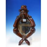 AN OVAL MIRROR IN MAHOGANY FRAME CARVED AS AS SEATED MAN HEAD IN HANDS AND WEARING A HAT. H 41cms.