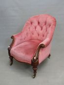 AN EARLY VICTORIAN BUTTON BACK ARMCHAIR WITH CARVED SHOW FRAME ARMS ON TURNED FORELEGS WITH BRASS