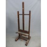A VINTAGE OAK EASEL, THE PICTURE RESTING CRANKING UP AND DOWN ON A WOODEN SCREW AND WITH FOLD OUT