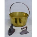 AN IRON HANDLED BRASS JAM PAN. Dia.38cms. TOGETHER WITH TWO IRON CLOTHES IRONS