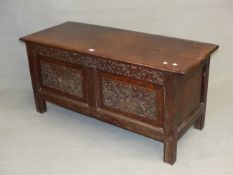 AN 18th C. OAK COFFER, THE TWO PLANK TOP HINGED OVER TWO PANELS TO THE FRONT CARVED WITH FOLIAGE.