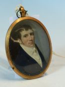 A GEORGIAN OVAL MINIATURE OF A GENTLEMAN IN YELLOW METAL MOUNT, INSET LOCK OF HAIR VERSO. 6.5 x