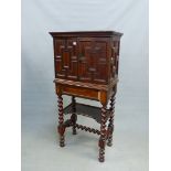 A 17th C. STYLE OAK CABINET ON STAND, THE GEOMETRICALLY PANELLED DOORS ENCLOSING DRAWERS AROUND A