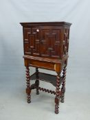 A 17th C. STYLE OAK CABINET ON STAND, THE GEOMETRICALLY PANELLED DOORS ENCLOSING DRAWERS AROUND A