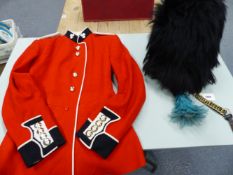 AN IRISH GUARDS REGIMENTAL TUNIC TOGETHER WITH A BUSBY WITH A BLUE PLUME TO ONE SIDE AND BRASS CHAIN