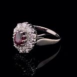 AN 18ct WHITE GOLD RUBY AND DIAMOND CLUSTER RING. THE OVAL CLAW SET RUBY SURROUNDED BY A CLUSTER