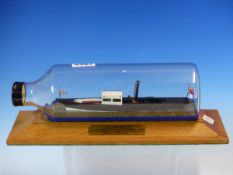 A SCALE MODEL OF THE WINDERMERE STEAM LAUNCH DOLLY WITHIN A BOTTLE ON AN OAK PLINTH. W 29cms.