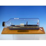 A SCALE MODEL OF THE WINDERMERE STEAM LAUNCH DOLLY WITHIN A BOTTLE ON AN OAK PLINTH. W 29cms.