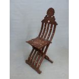 AN ISLAMIC INTAGLIO CARVED HARDWOOD FOLDING CHAIR, THE BARS OF THE BACK AND FRONT LEG INTERLOCKING