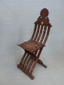 AN ISLAMIC INTAGLIO CARVED HARDWOOD FOLDING CHAIR, THE BARS OF THE BACK AND FRONT LEG INTERLOCKING