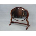 AN OVAL DRESSING TABLE MIRROR WITH MAHOGANY CURVED SUPPORTS BEARING BRASS FITTING FOR CANDLESTICKS