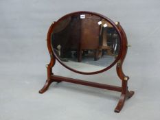 AN OVAL DRESSING TABLE MIRROR WITH MAHOGANY CURVED SUPPORTS BEARING BRASS FITTING FOR CANDLESTICKS