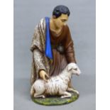 A CERAMIC FIGURE OF A SHEPHERD KNEELING BY A SHEEP, HIS BLUE LINED CLOAK OVER HIS RIGHT