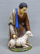 A CERAMIC FIGURE OF A SHEPHERD KNEELING BY A SHEEP, HIS BLUE LINED CLOAK OVER HIS RIGHT