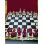 A RED AND WHITE BONE BARLEYCORN CHESS SET ON PAINTED FOLD OVER BOARD, THE KINGS. H 8.5cms.