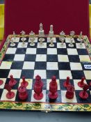 A RED AND WHITE BONE BARLEYCORN CHESS SET ON PAINTED FOLD OVER BOARD, THE KINGS. H 8.5cms.