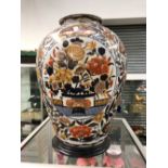A LARGE ORIENTAL STYLE BALUSTER VASE IN IMARI PALETTE COLOURS WITH WOODEN BASE.