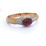 AN ANTIQUE GOLD AND ENAMEL ARTICULATED BANGLE, SET WITH AN OVAL RED CABOCHON, FINELY ENGRAVED WITH A