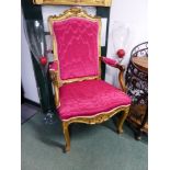 A RED SILK UPHOLSTERED FRENCH GILT WOOD ELBOW CHAIR, THE FLORAL CARVED SERPENTINE TOP RAIL OVER