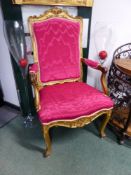 A RED SILK UPHOLSTERED FRENCH GILT WOOD ELBOW CHAIR, THE FLORAL CARVED SERPENTINE TOP RAIL OVER